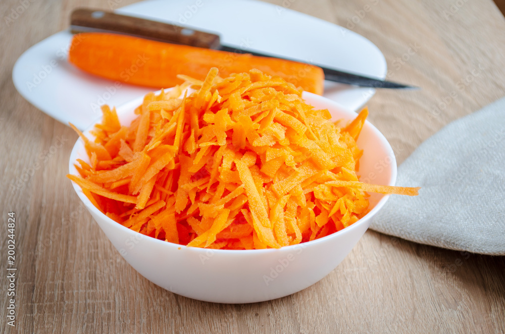 Grated carrots and whole carrot. White tableware and knife. Grated carrots and whole carrot. White tableware and knife.