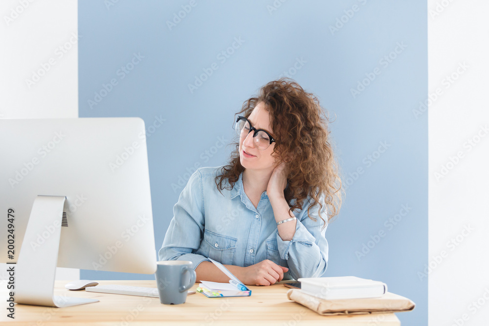Overworked female student has pain in neck, has fatigue expression, works all day on course paper Overworked female student has pain in neck, has fatigue expression, works all day on course paper