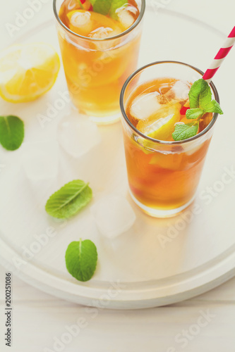 Glasses of iced tea with lemon slices and mint on white wooden background. Toned