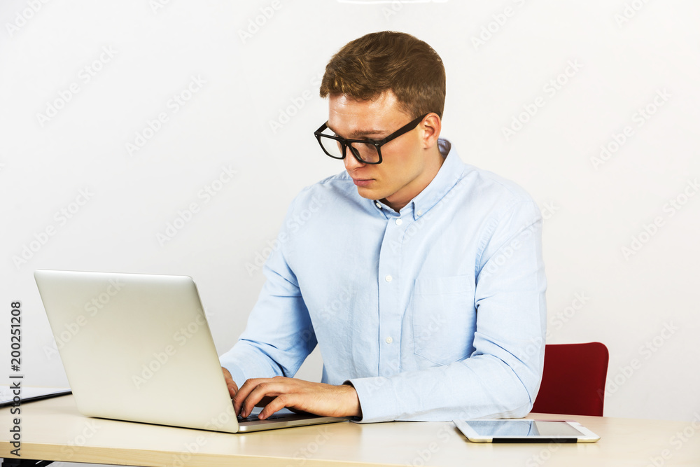 Happy young businessman using laptop at his office desk and using computer, glasses.