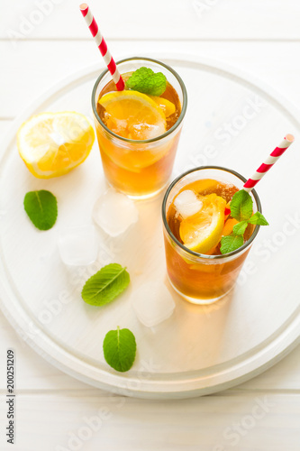 Glasses of iced tea with lemon slices and mint on white wooden background