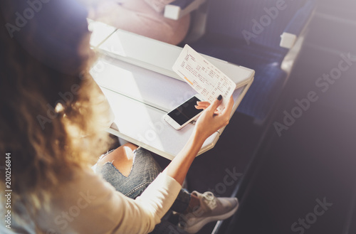 Enjoying business travel concept. Young beautiful brunette tourist girl travelling on the train sitting near the window using smartphone,holding ticket hands. photo