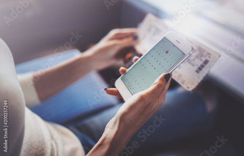 Enjoying business travel concept. Young beautiful brunette tourist girl travelling on the train sitting near the window using smartphone holding ticket hands.Horizontal closeup.