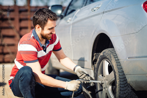 Smiling man and mechanic changing tyres, using jack and wheel wrench