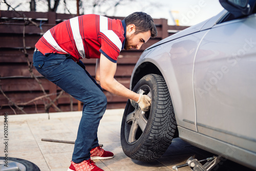 Potrait of young man changing seasonal tires, installing summer tires on automobile photo