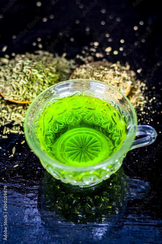 Closes up of essential tea of raw fresh fennel seeds with raw fennel seeds in a transparent cup on wooden surface for good skin and inhibits muscles spasms and helps for a good digestion. Closes up of essential tea of raw fresh fennel seeds with raw fennel seeds in a transparent cup on wooden surface for good skin and inhibits muscles spasms and helps for a good digestion.