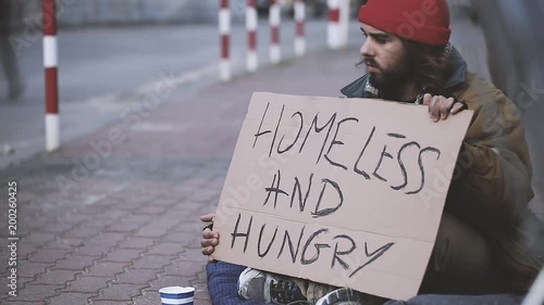 Time lapse video of a homeless and hungry beggar sitting on the sidewalk on which pedestrians are walking in the city photo