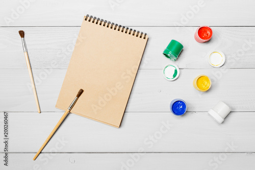 Gouache watercolor paint. Drawing paintbrush on paper notebook. White wooden background