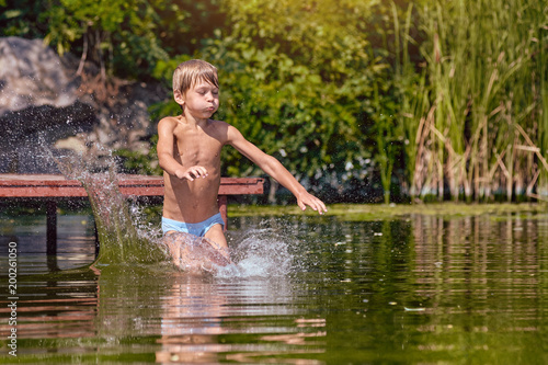 Little boy having fun and jumping into the river from pier