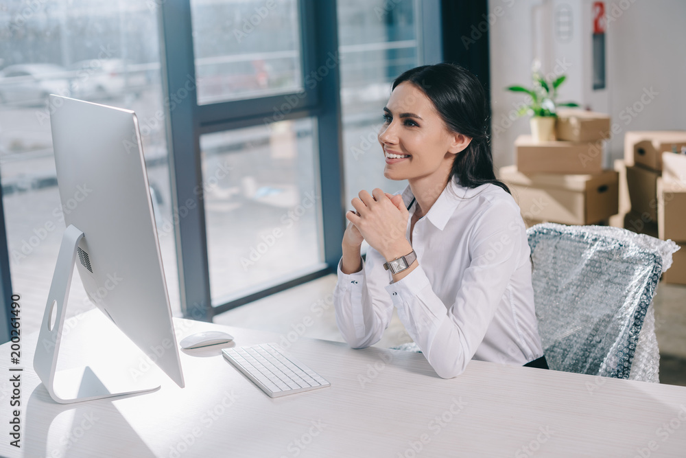 happy young businesswoman using desktop computer while sitting at workplace in new office happy young businesswoman using desktop computer while sitting at workplace in new office