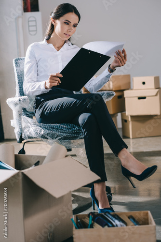 focused young businesswoman holding clipboard while sitting in new office during relocation © LIGHTFIELD STUDIOS