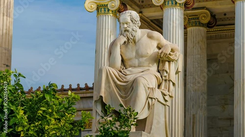 Statue of the Greek philosopher Socrates on a marble chair, background of columns and sky.
