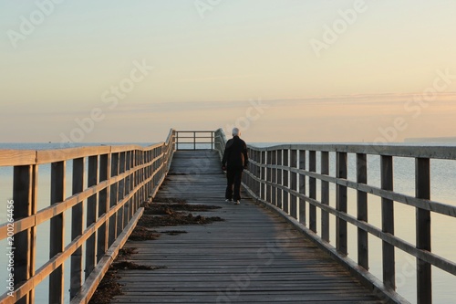 athletic old senior with dumbbells walks along a pier 