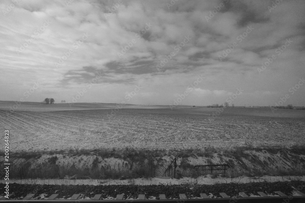 beautiful black and white winter landscape with  cloudy sky, frosty fields and trees in the background, with railroad trucks on a sunny day in Poland, Europe