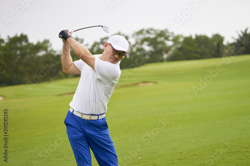 Asian golfer swinging club in golf course for tee off