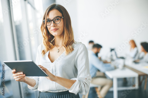 Elegant businesswoman standing in office with digital tablet photo