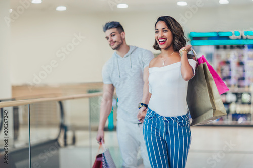 Happy young couple with shopping bags walking in mall - sale, consumerism and people concept photo