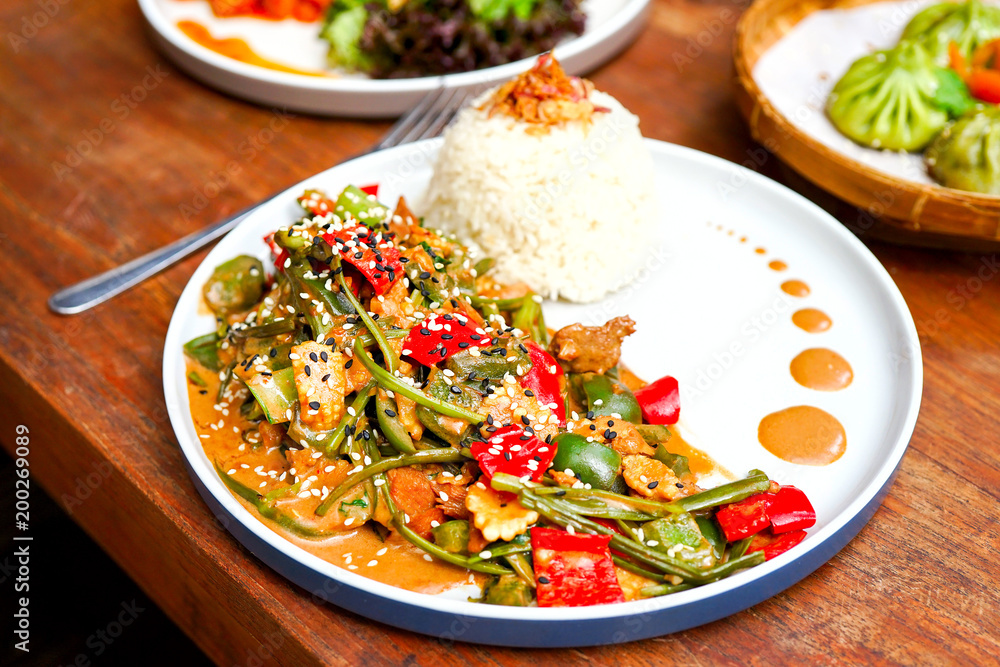 Chicken kung pao on a white plate and on a light wooden table. Chinese food. Food sticks. On the back of a blurry background, a white brick pad is covered with an word love. Side view with copy space Chicken kung pao on a white plate and on a light wooden table. Chinese food. Food sticks. On the back of a blurry background, a white brick pad is covered with an word love. Side view with copy space