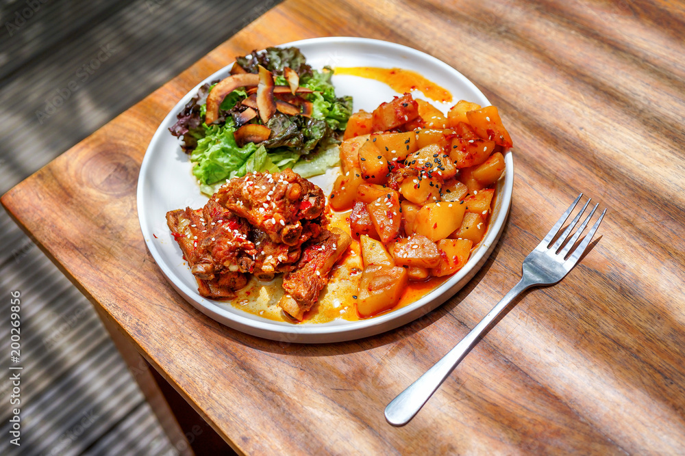 Fried pork ribs with potatoes and salad. On a white plate with a knife and fork. Wooden background - a table. Top view with copy space Fried pork ribs with potatoes and salad. On a white plate with a knife and fork. Wooden background - a table. Top view with copy space