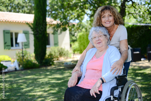 cheerful mature woman visiting her mother elderly senior female on wheel chair in retirement house hospital garden