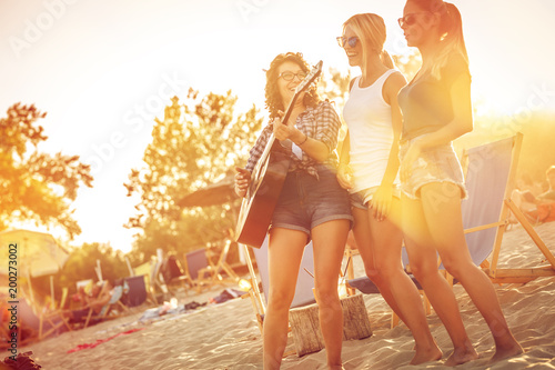 Group of young female friends  on beach  singing and playing guitar.Joying in sunset.