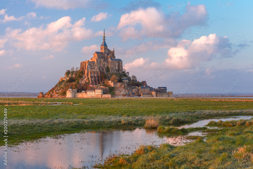 Beautiful famous Mont Saint Michel at sunset with reflection in the canal on the water meadows, Normandy, France