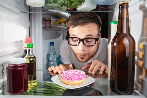 Mann betrachtet einen Donut im Kühlschrank photo