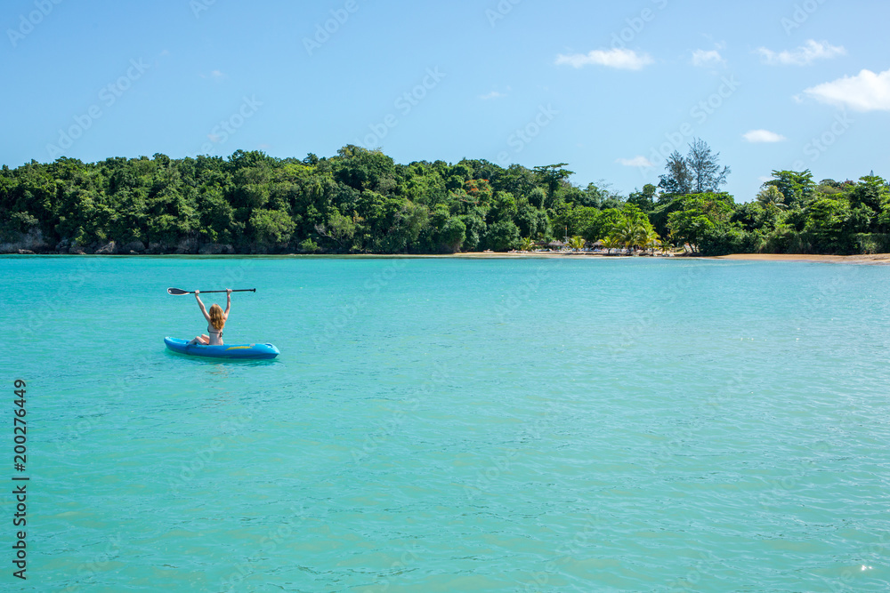 Eine junge Frau paddelt in einem Kajak auf dem Meer in der Karibik auf Jamaika
