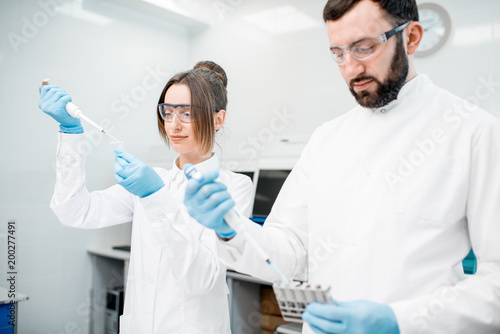 Couple of laboratory assistants in uniform working with analysis in test tubes at the medical laboratory