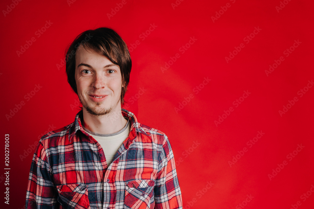 Fototapeta premium Portrait of a man in a plaid shirt on a red background, the man smiles at the camera, copy space