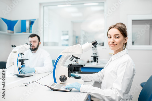 Portrait of two medics in uniform working with microscope making analysis at the laboratory office
