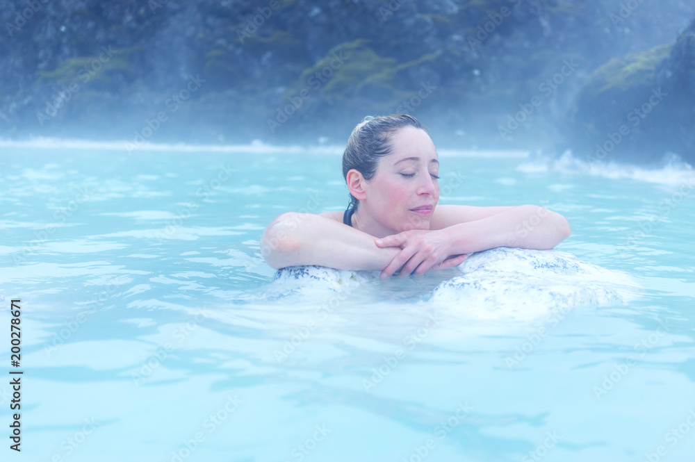 woman resting with eyes closed on a rock in a hot spring