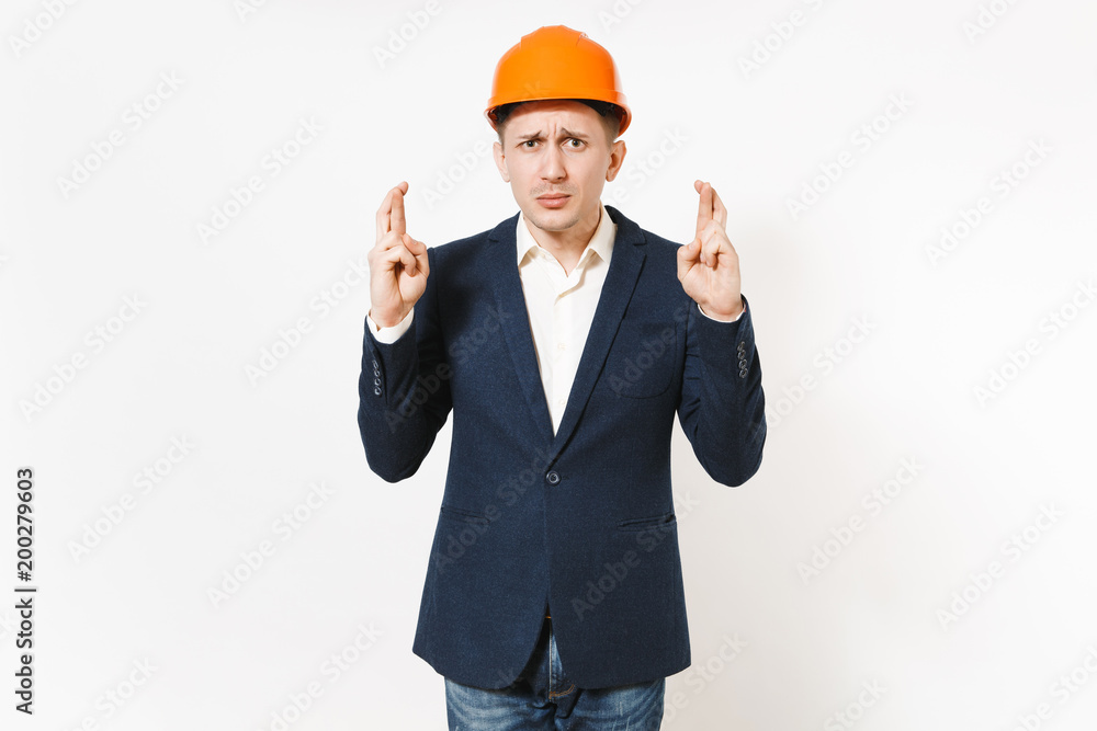 Concerned businessman in dark suit, protective construction helmet keeping fingers crossed and waiting for special moment isolated on white background. Making a wish. Male worker for advertisement.