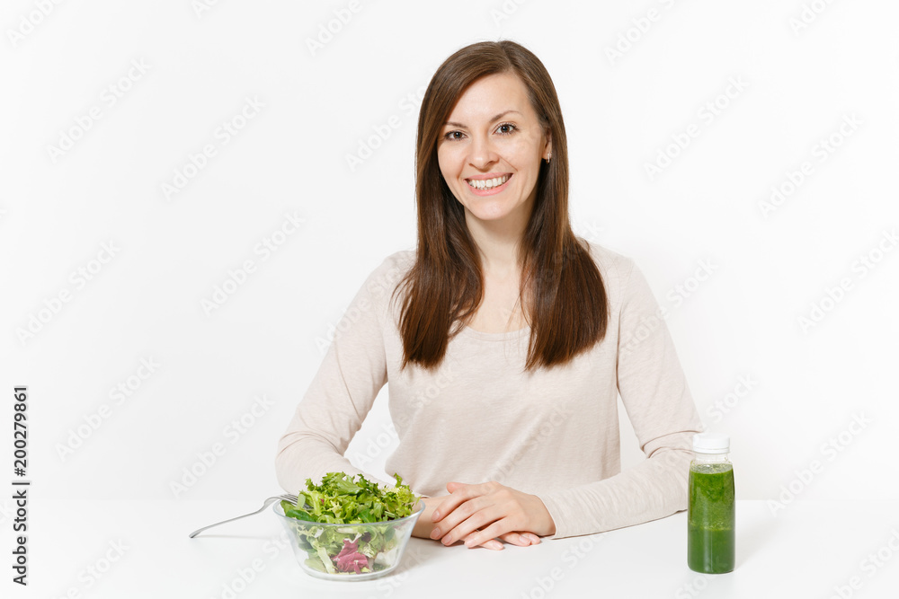 Young woman sitting at table with green detox smoothies, salad in glass bowl isolated on white background. Proper nutrition, vegetarian food, healthy lifestyle, dieting concept. Area with copy space. Young woman sitting at table with green detox smoothies, salad in glass bowl isolated on white background. Proper nutrition, vegetarian food, healthy lifestyle, dieting concept. Area with copy space.