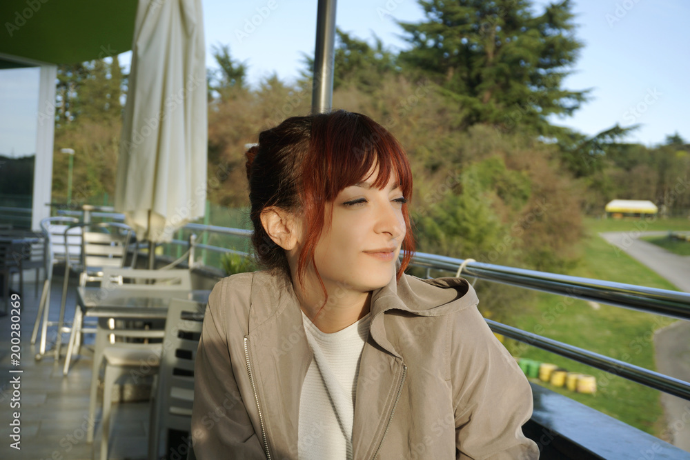 Beautiful and smart young woman sitting on the cafe terrace and satisfied looking into the distance Beautiful and smart young woman sitting on the cafe terrace and satisfied looking into the distance