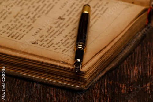 old book and an ink pen on a wooden background.