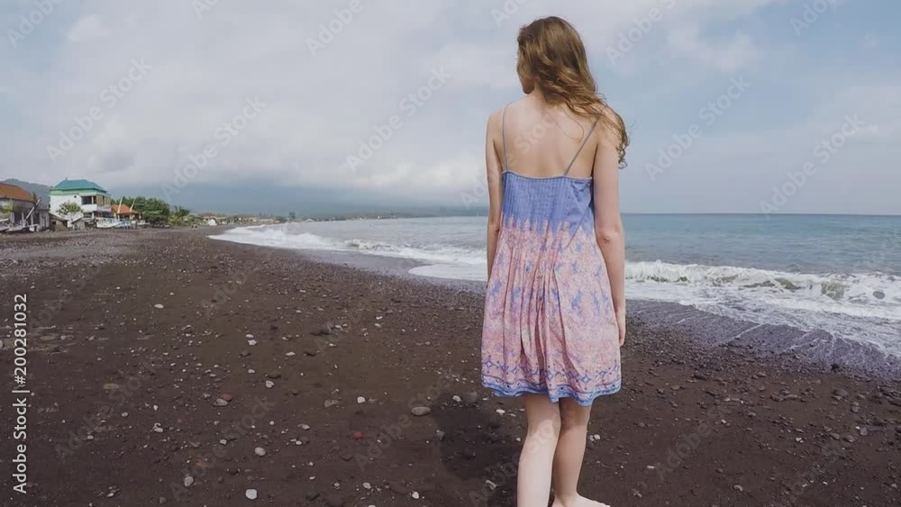 Beautiful girl looks around on a black beach of volcanic sand Beautiful girl looks around on a black beach of volcanic sand