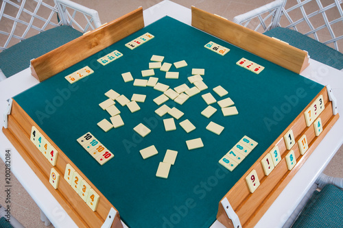 Turkish board game Okey (Rummikub). A table with green cloth and chips. Hands of the players. photo