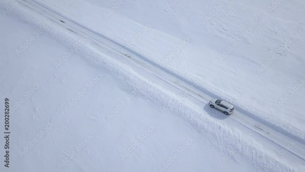 Aerial view on car driving through winter forest road between the snow-covered fields Aerial view on car driving through winter forest road between the snow-covered fields