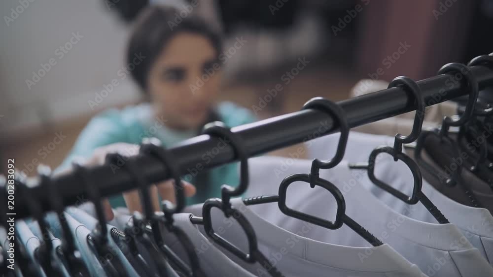 Woman choise clothes in shop, focus on hangers Woman choise clothes in shop, focus on hangers
