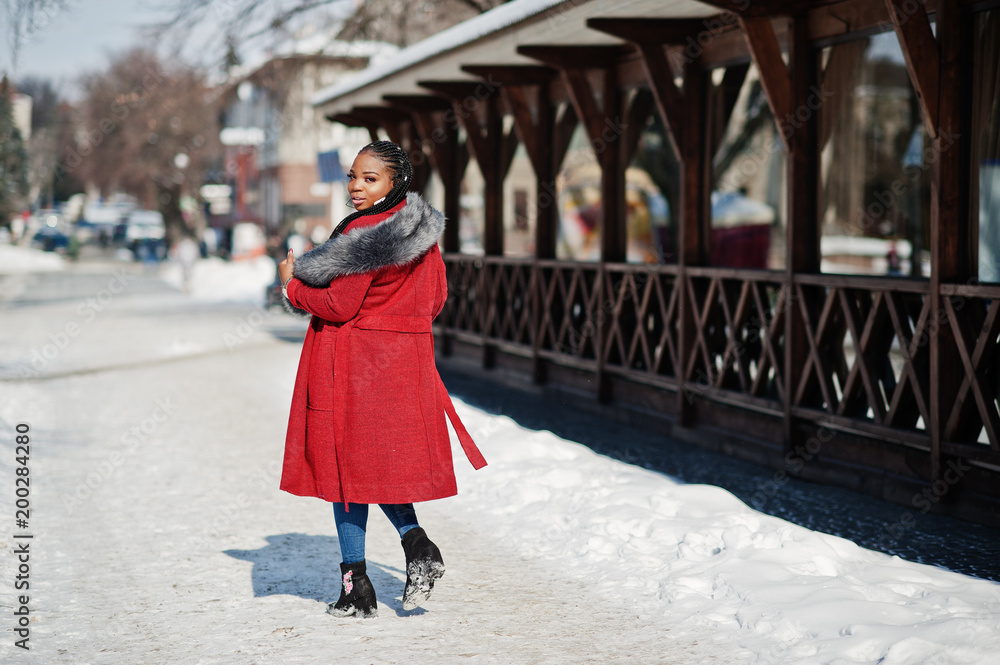Back of walking rich african american girl in red coat and fur on winter street at sunny weather. Black stylish woman.