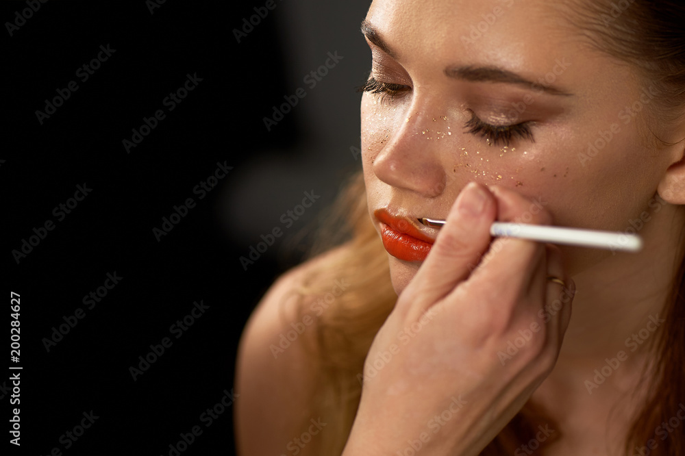 Obraz premium Portrait of young beautiful girl in Studio, with professional makeup. Beauty shooting. Makeup artist paints her lips with a brush