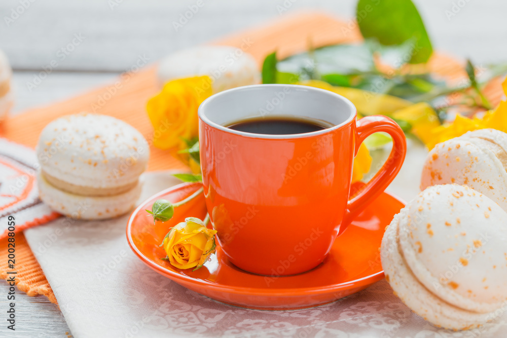 Orange cup of black coffee, yellow roses flowers and sweet pastel french macaroons Orange cup of black coffee, yellow roses flowers and sweet pastel french macaroons