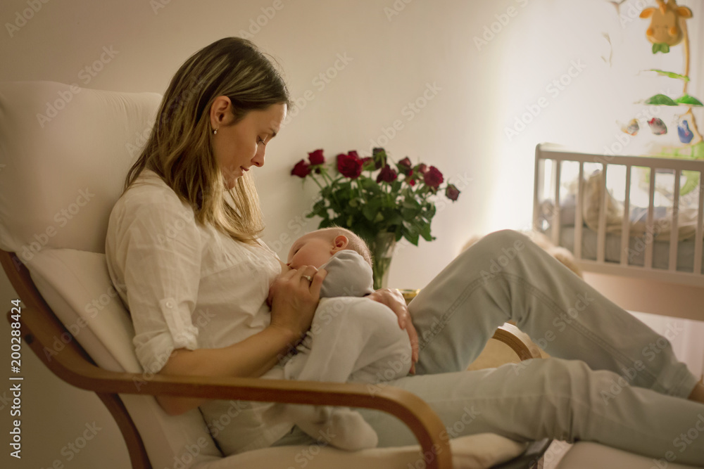 Young beautiful mother, breastfeeding her newborn baby boy at night, dim light Young beautiful mother, breastfeeding her newborn baby boy at night, dim light