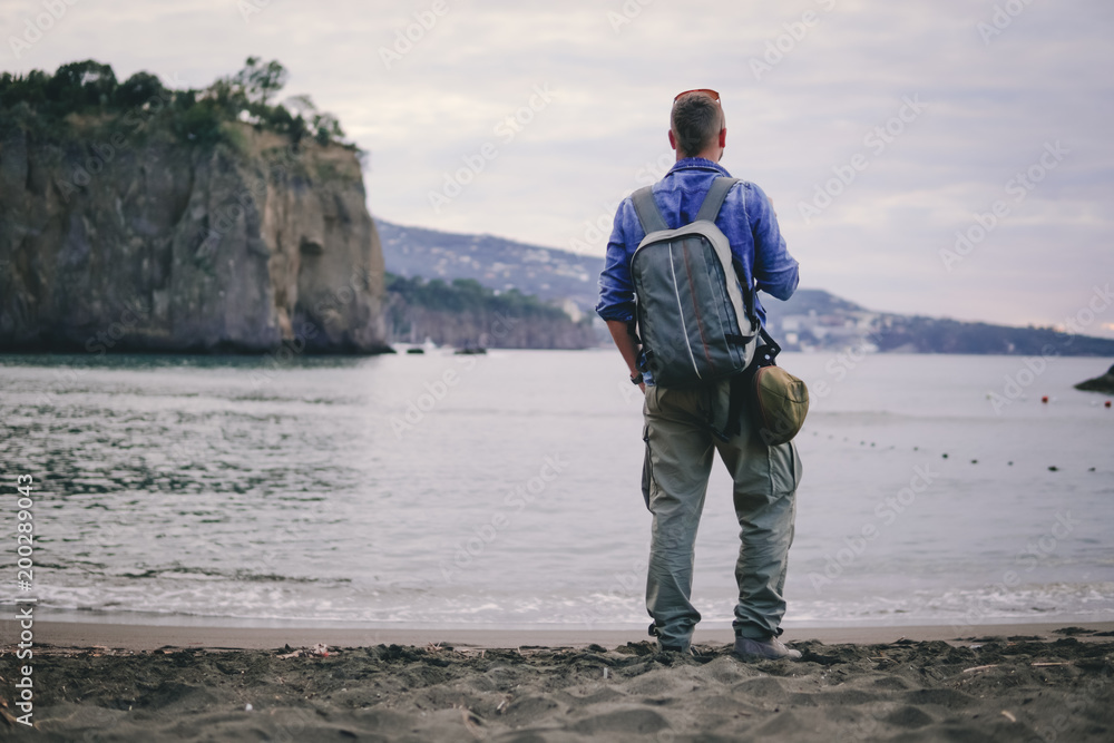 man, guy the photographer working look at the phone, receives a call, calls on the beach, backpack, concept of find information at travel to foregin country, communication, mountains on background