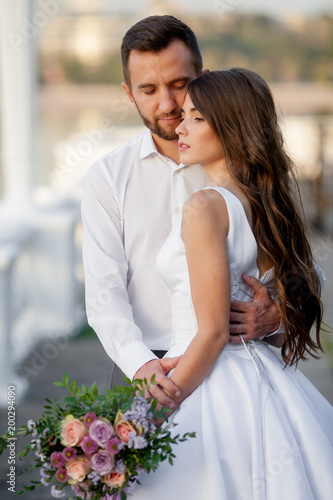 A groom and a bride sensually embrace near the lake