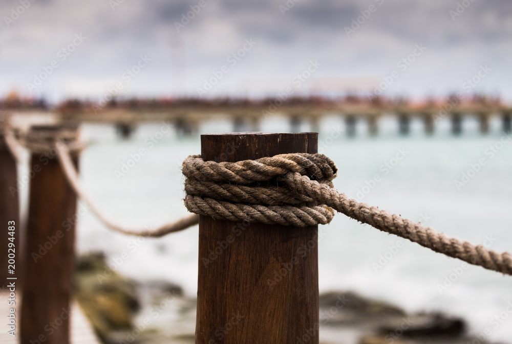 Obraz premium Close-up view of a pole on a rope bridge in Mexico with a port pier in the background