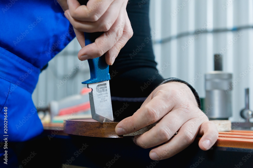 Obraz premium A close-up of the real male carpenter's not well-groomed hands completes the finish of the chipboard details of the furniture by cutting off the edge of the edge of the stripped decorative strip. The