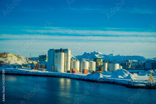 Outdoor view of industrial port area  showing ships and herring oil production plant during a winter season and blue sky  in port of Bodo  Norway