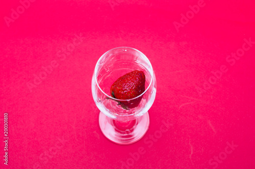 Ripe strawberries in a wine glass on red background